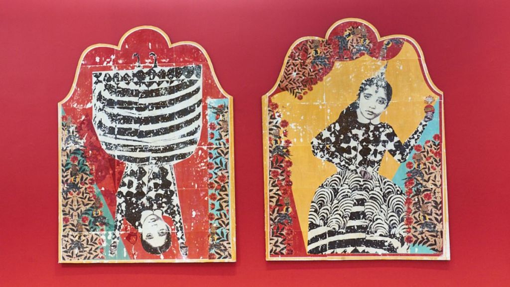 A pair of prints on panels with scalloped tops, each showing a female figure with a body constructed of abstract calligraphic marks, in black & white, yellow and blue, hung on a wall painted deep red